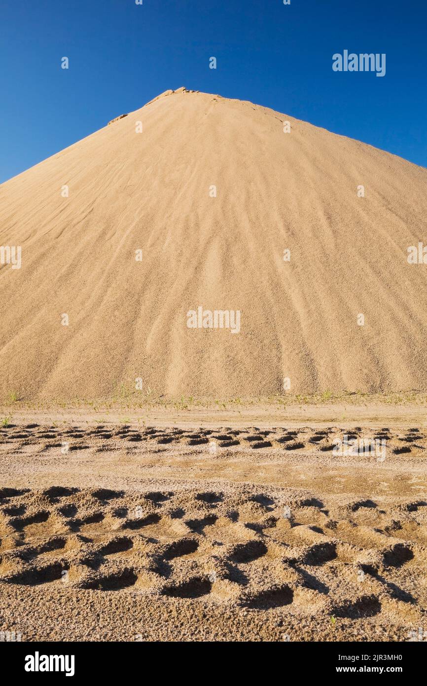 Heavy tire tracks and a mound of stacked tan colored sand in a commercial sandpit. Stock Photo