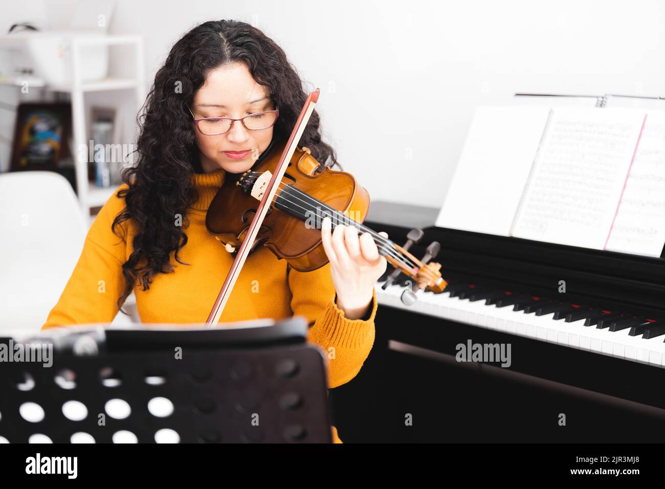 Eyes closed brunette concert woman wearing a yellow sweater, and playing violin by reading sheet music. Stock Photo
