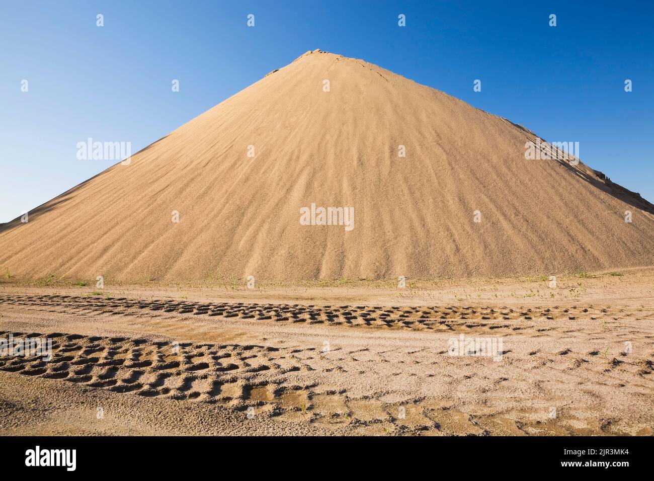 Heavy tire tracks and a stacked mound of tan colored sand in a commercial sandpit. Stock Photo