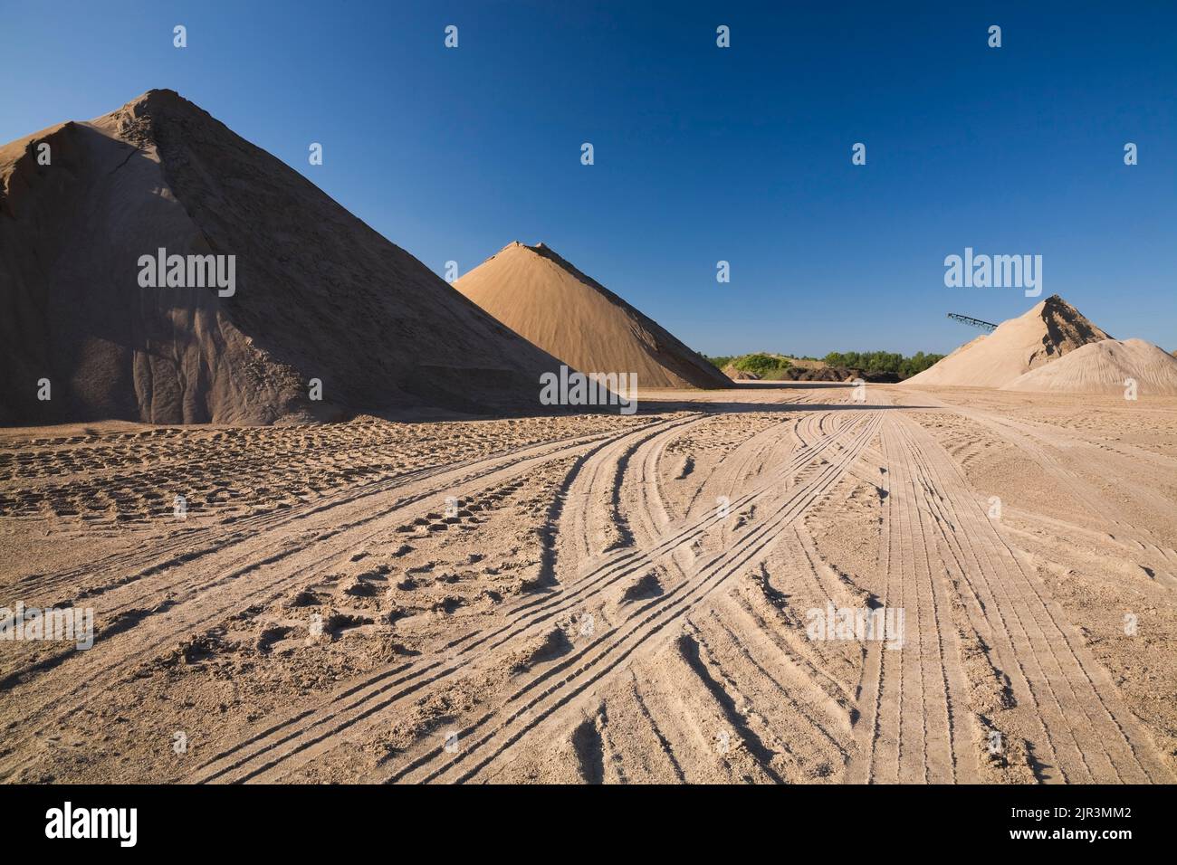 Tire tracks and stacked mounds of light brown and tan colored sand in a commercial sandpit. Stock Photo