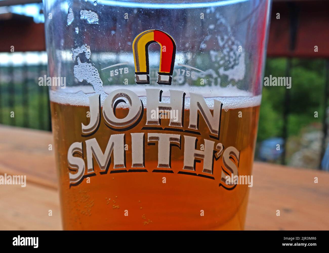 John Smiths, Magnet Ales, pint glass, ESTB 1758, half-full of beer, Llangollen, North Wales, UK - the highest selling bitter in the United Kingdom Stock Photo