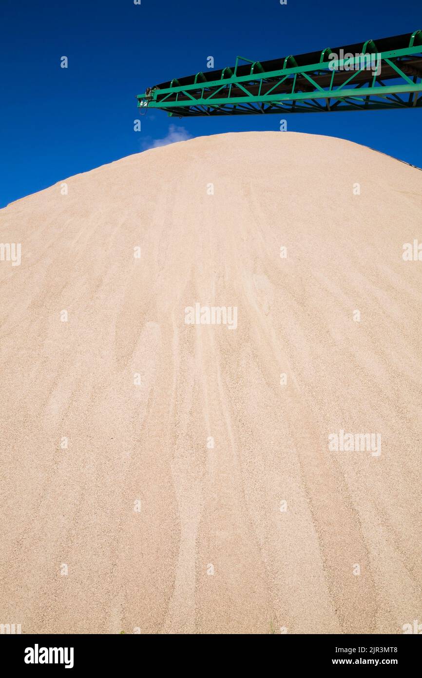 Green stacking conveyor and mound of tan sand in a commercial sandpit. Stock Photo