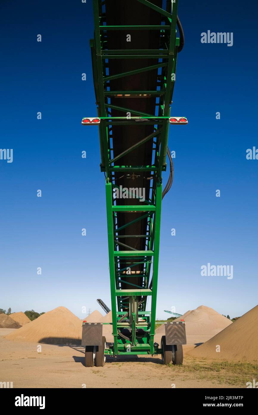 Green stacking conveyor and mounds of tan and light brown sand in a commercial sandpit. Stock Photo