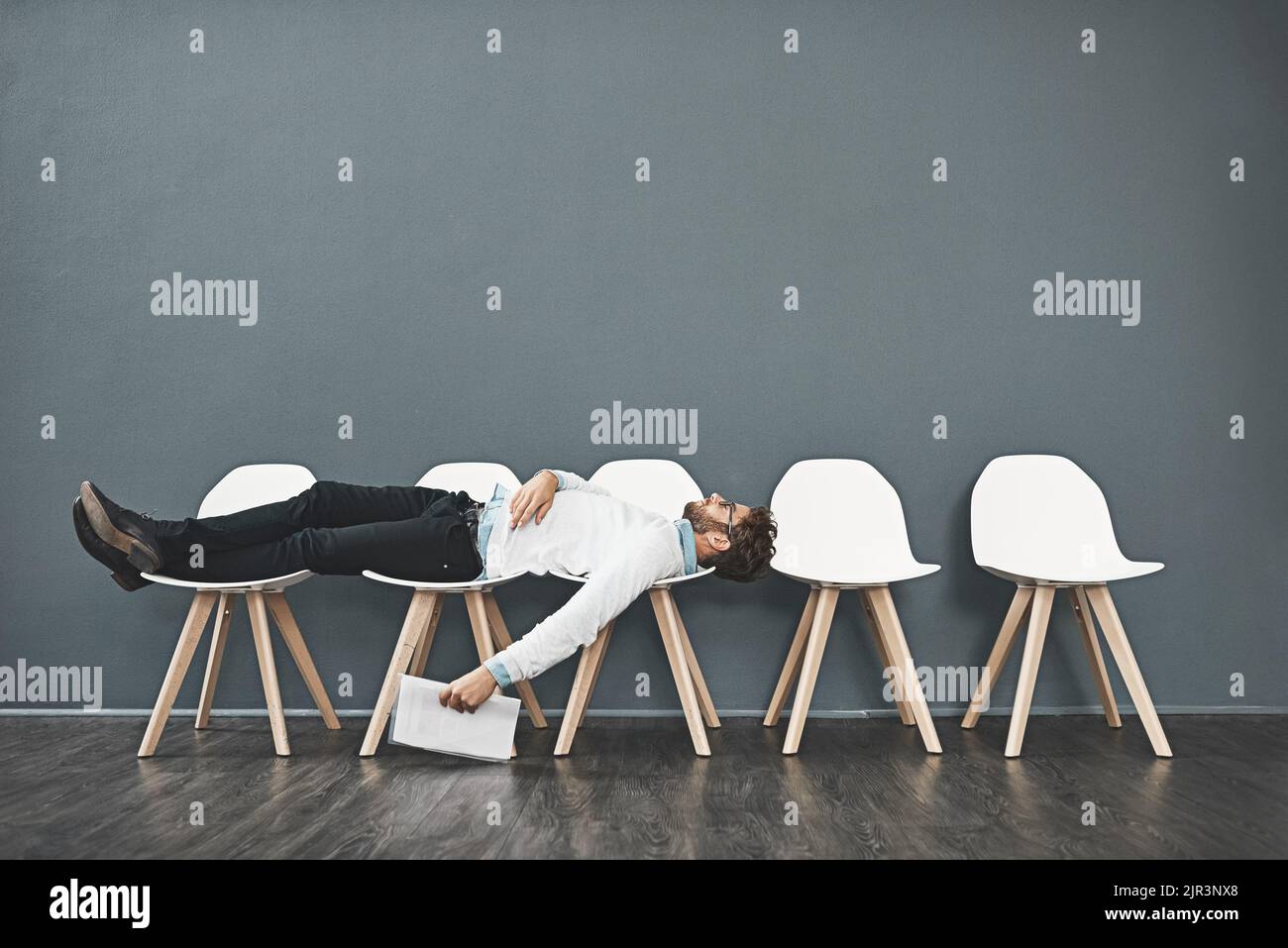 Can this wait get any longer. a young man lying down on a row of chairs while waiting in line for a job interview. Stock Photo