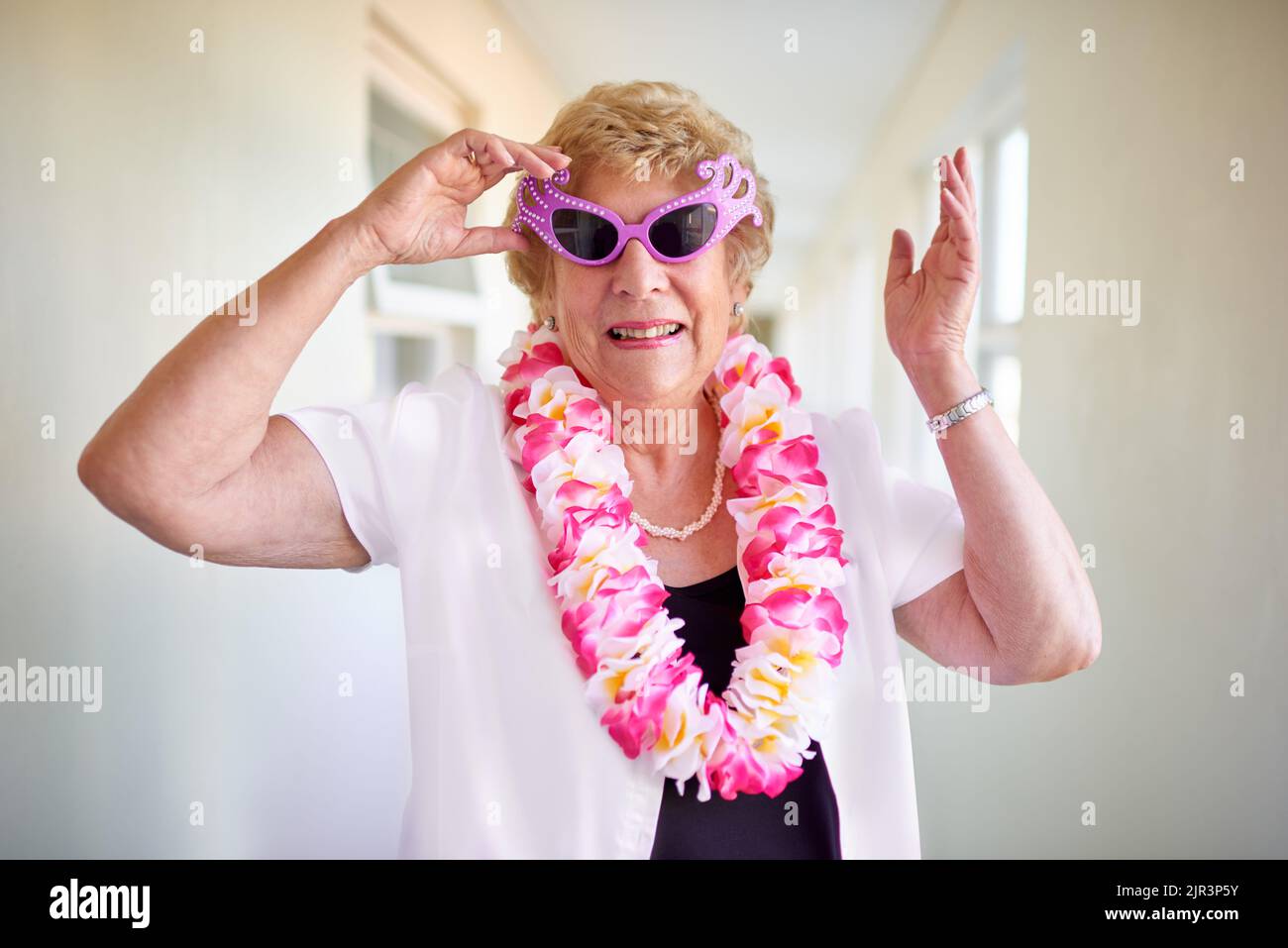 I still have fun at my age. a carefree elderly woman wearing pink glasses and posing inside of a building. Stock Photo