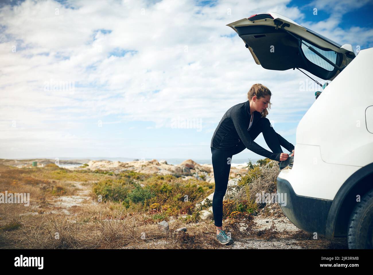 Car boots make for a great stand to tie shoelaces. a young woman tying