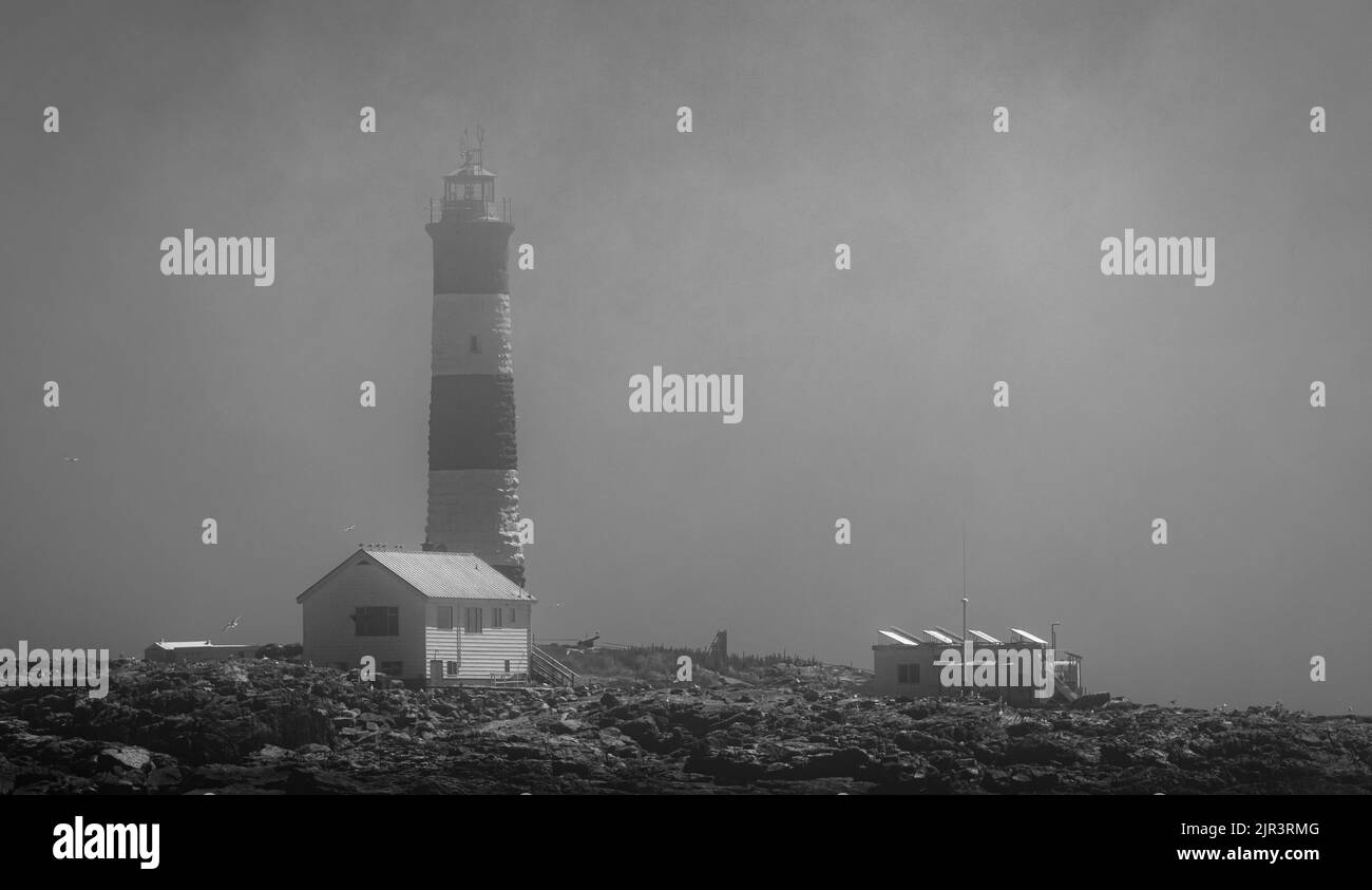 Beautiful lighthouse on the top of a rocky mountain with sea in foggy morning in black and white Stock Photo