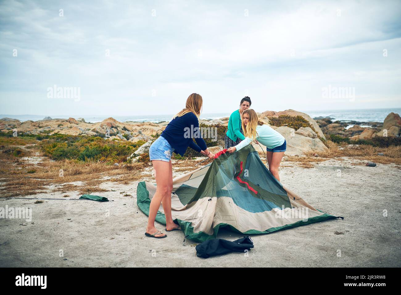 We all pitch in to set up the tent. a group of female friends setting up a tent outdoors. Stock Photo
