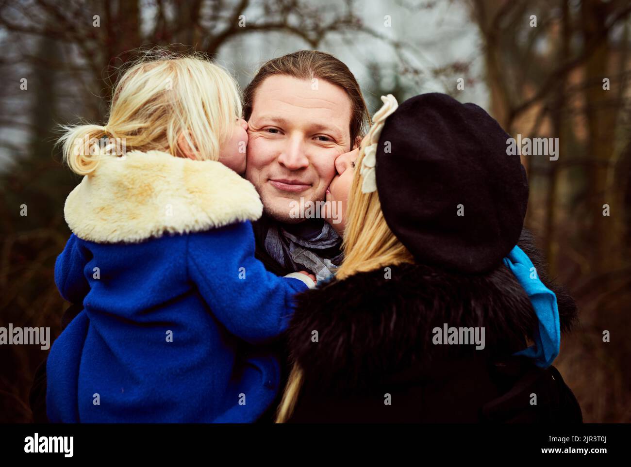 Kisses from my two favourite girls. a mother and daughter kissing the father on the cheeks outdoors. Stock Photo