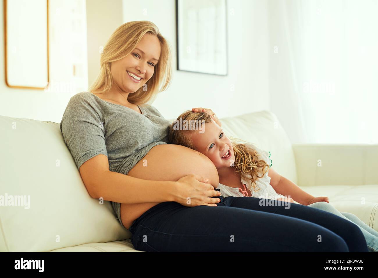 Were both excited about this pregnancy. a little girl listening to her mothers pregnant belly. Stock Photo