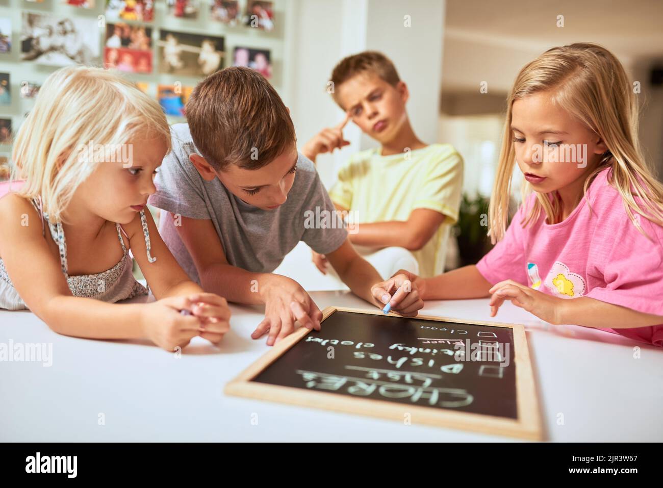 Doing chores teaches kids to take responsibility. kids writing a list of chores on a chalkboard at home. Stock Photo