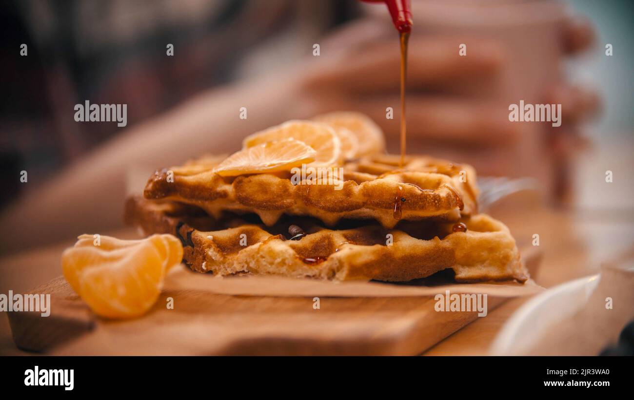 Covering a belgian waffle surrounded by mandarin slices with a syrup - cafe kitchen Stock Photo