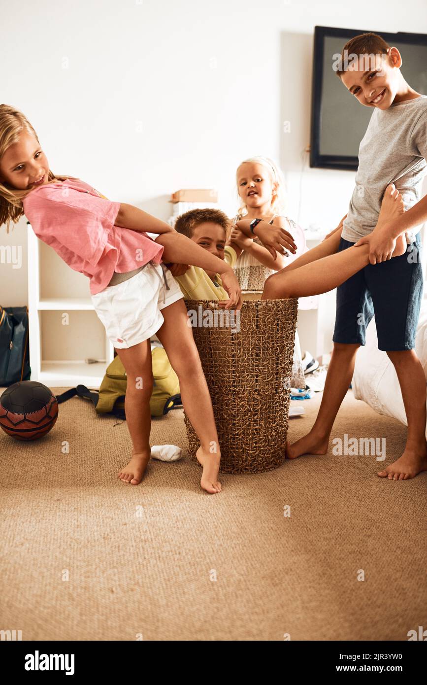 Oh no, hes stuck. Portrait of little siblings pulling their brother out a laundry basket at home. Stock Photo