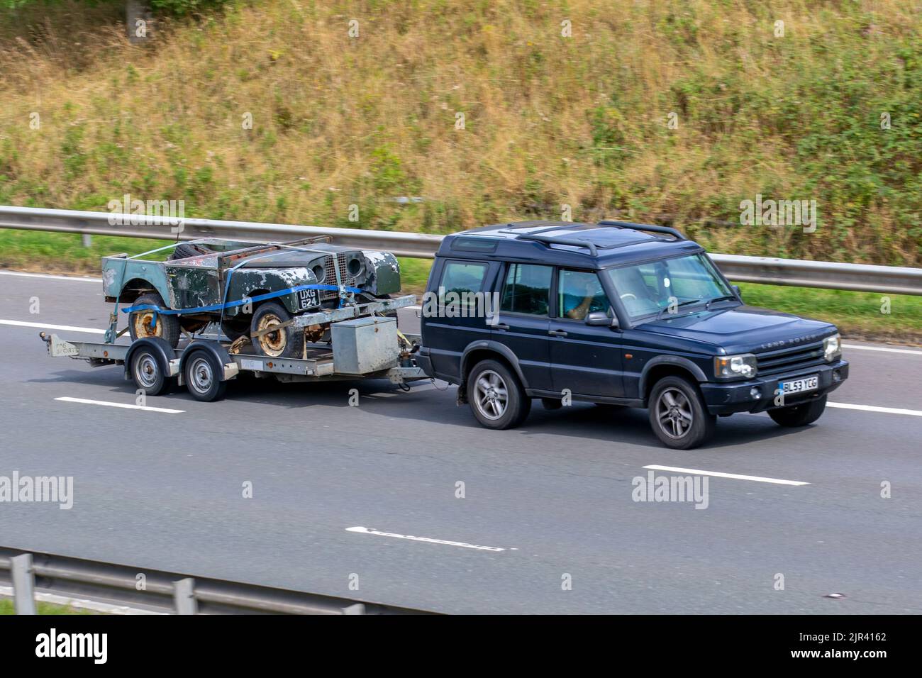 1952 Series II 2a Land Rover Body Shell restoration project on car trailer being towed by 2004 blue Land Rover Discovery. car carrier, transporting, car haulier, tow vehicle, car-carrying trailer, auto transport trailer, semi-trailer on the M6 Motorway, UK travelling on the M6 motorway, UK Stock Photo
