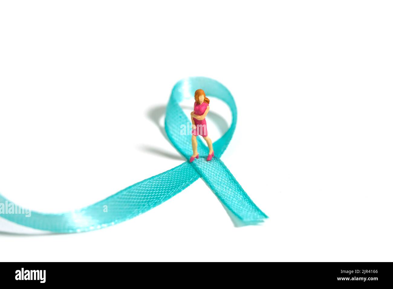 Miniature people figure toys photography. Ovarian and breast cancer awareness day concept. Girl, teenage, woman standing above green turquoise teal ri Stock Photo