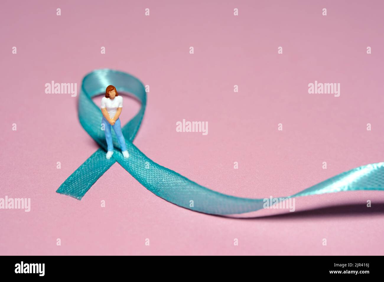 Miniature people figure toys photography. Ovarian cancer awareness day concept. Girl, teenage, woman standing above green turquoise teal ribbon. Image Stock Photo