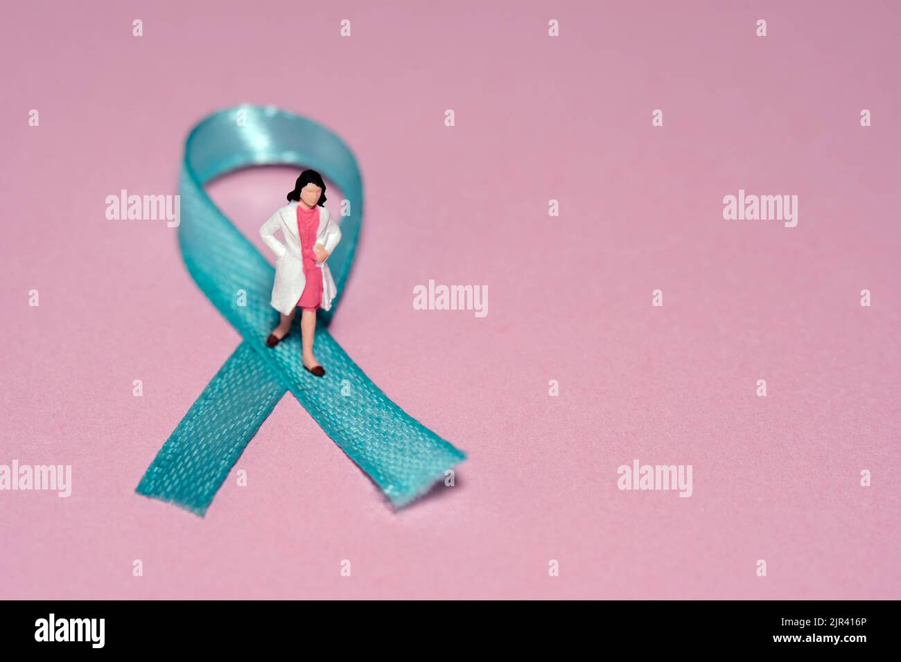 Miniature people figure toys photography. Ovarian cancer awareness day concept. Girl woman doctor standing above green turquoise teal ribbon. Image ph Stock Photo