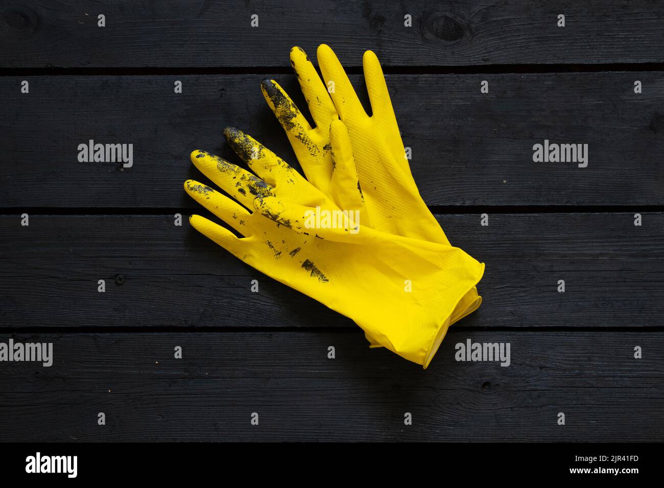 yellow rubber gloves in black paint on a black wooden floor, gloves in
