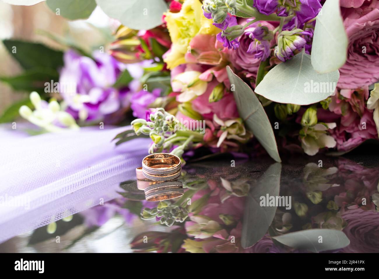 two wedding gold rings on a dark mirror background carried a bouquet of flowers, wedding gold rings, wedding Stock Photo