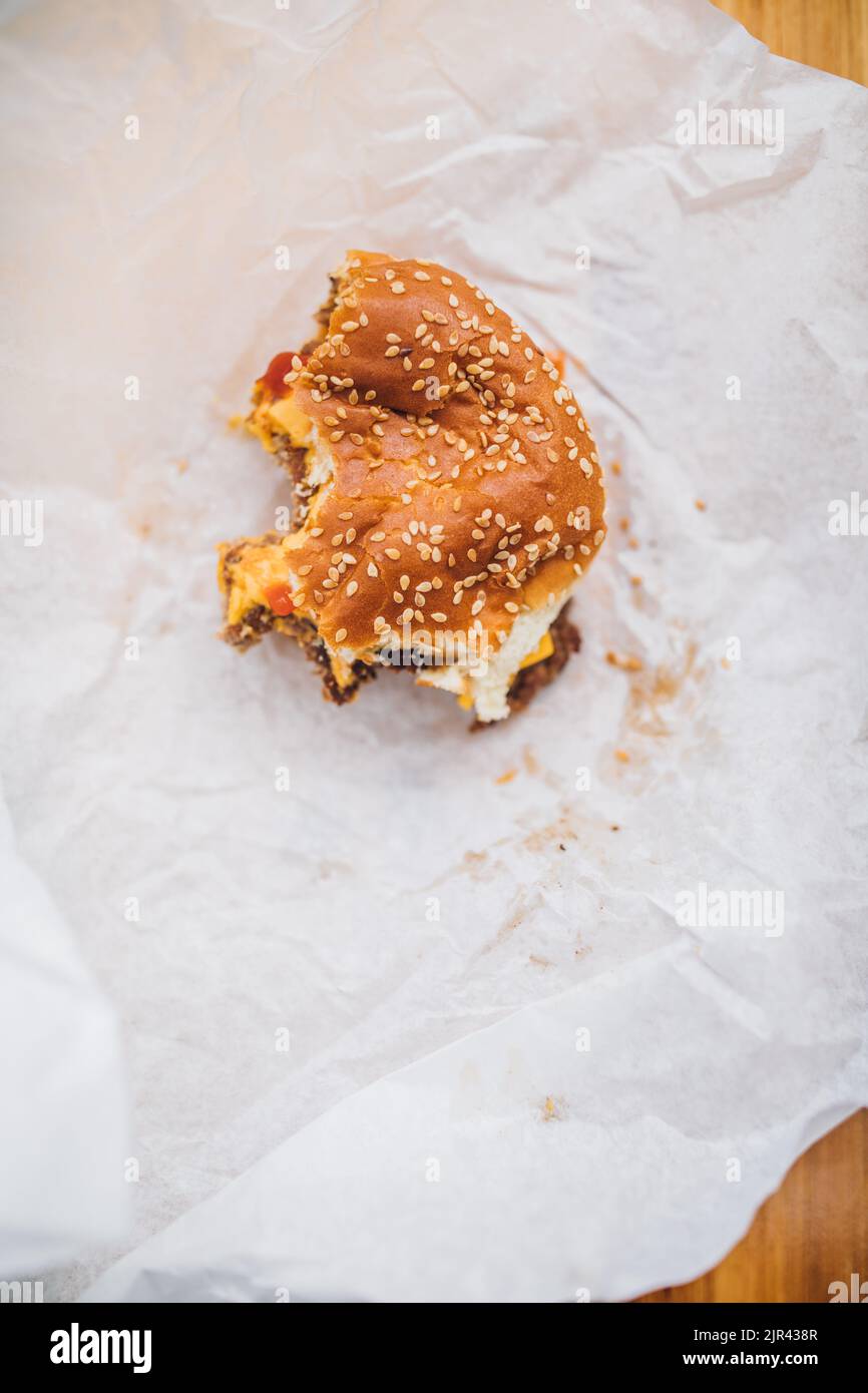 half eaten cheeseburger with sesame bun on white paper Stock Photo