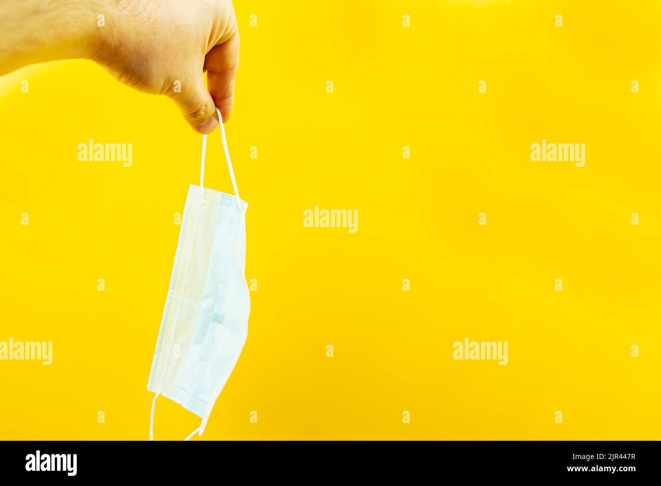 A hand holding a medical protective mask on a yellow background. Virus protection. An epidemic. Stock Photo