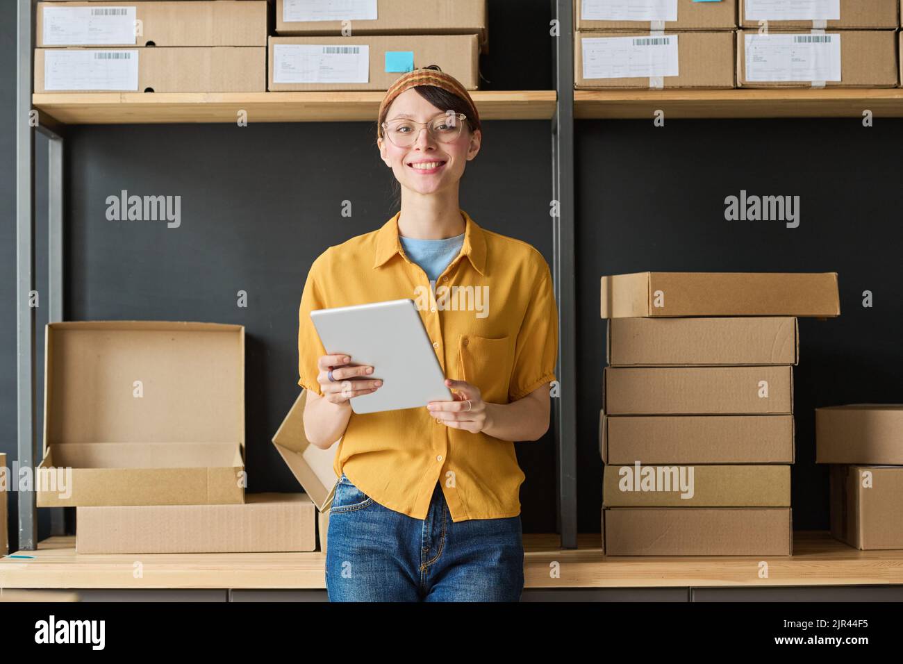 Portrait of young woman smiling at camera while using digital tablet in warehouse Stock Photo