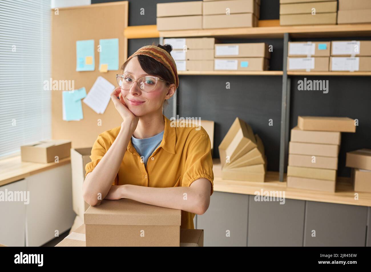Portrait of female warehouse worker looking at camera while packing parcels in storage Stock Photo