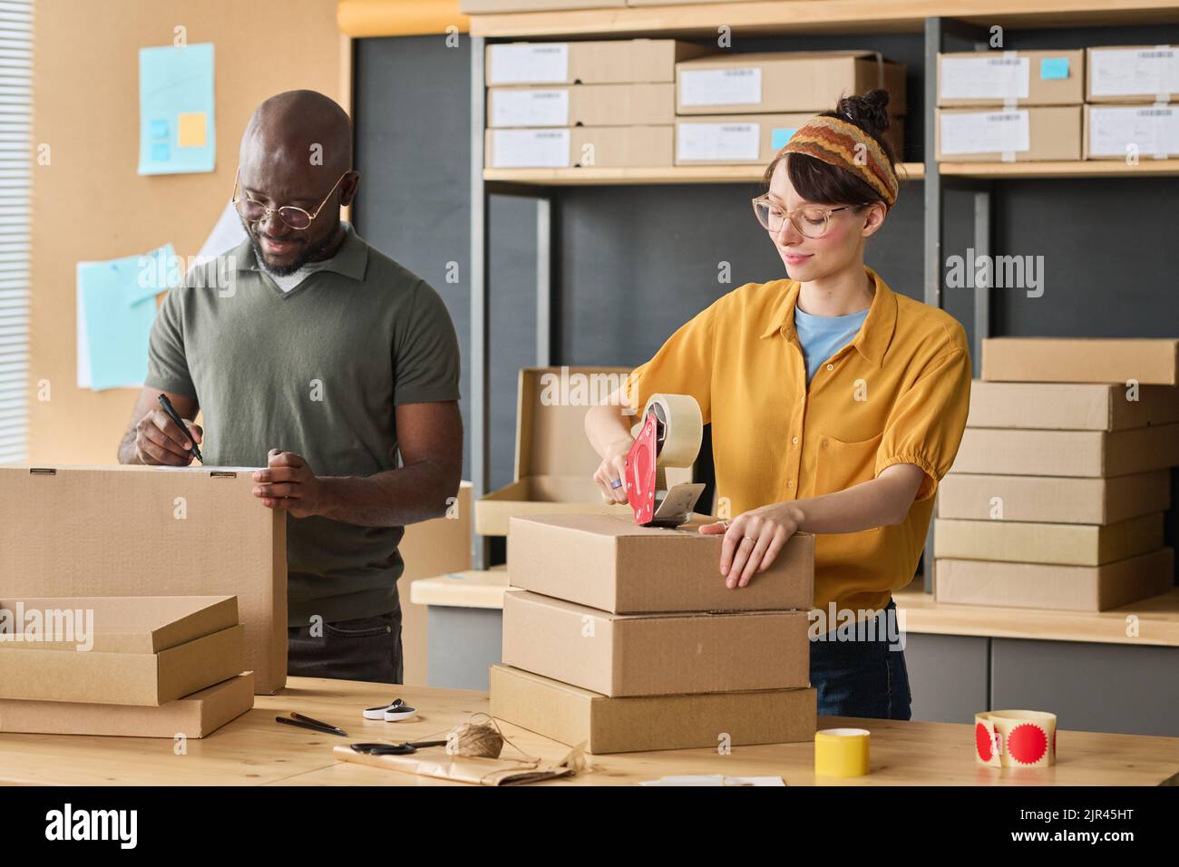 Multiethnic couple of workers packing parcels in cardboard boxes together before shipping Stock Photo