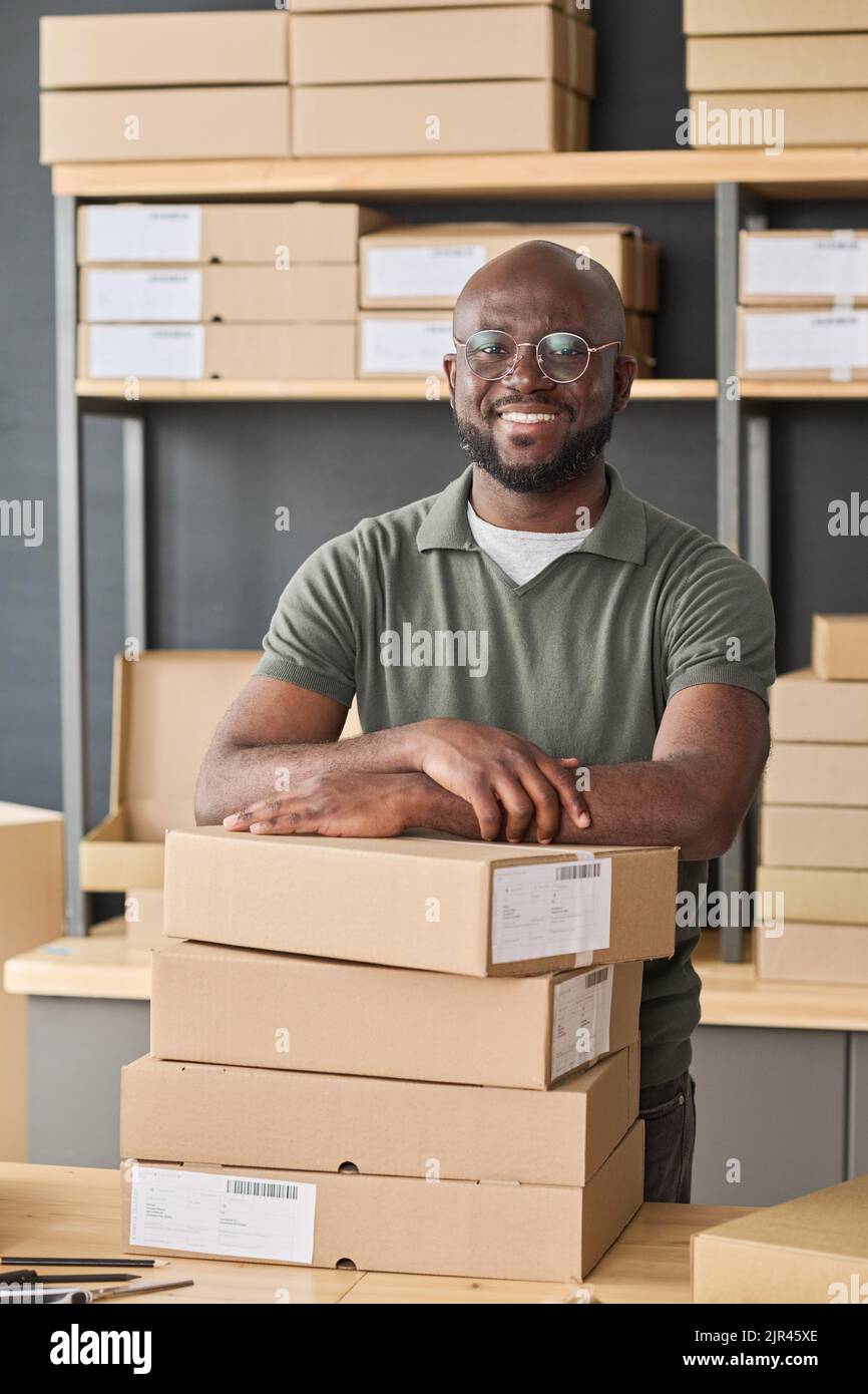 Portrait of African warehouse worker in eyeglasses smiling at camera while distributing parcels in warehouse Stock Photo