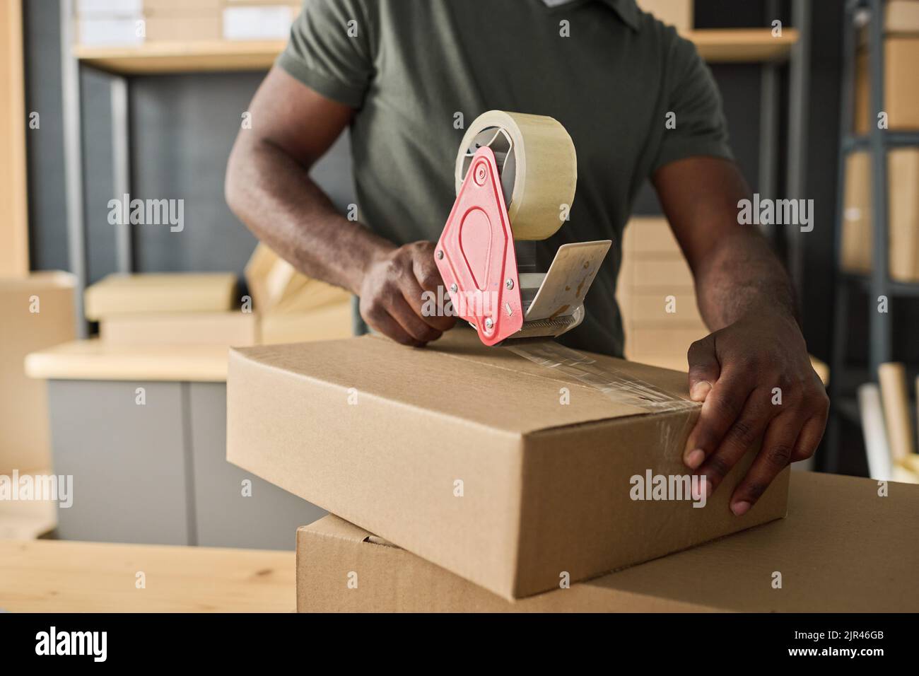 Close-up of African man packing cardboard box with adhesive tape in storage room Stock Photo