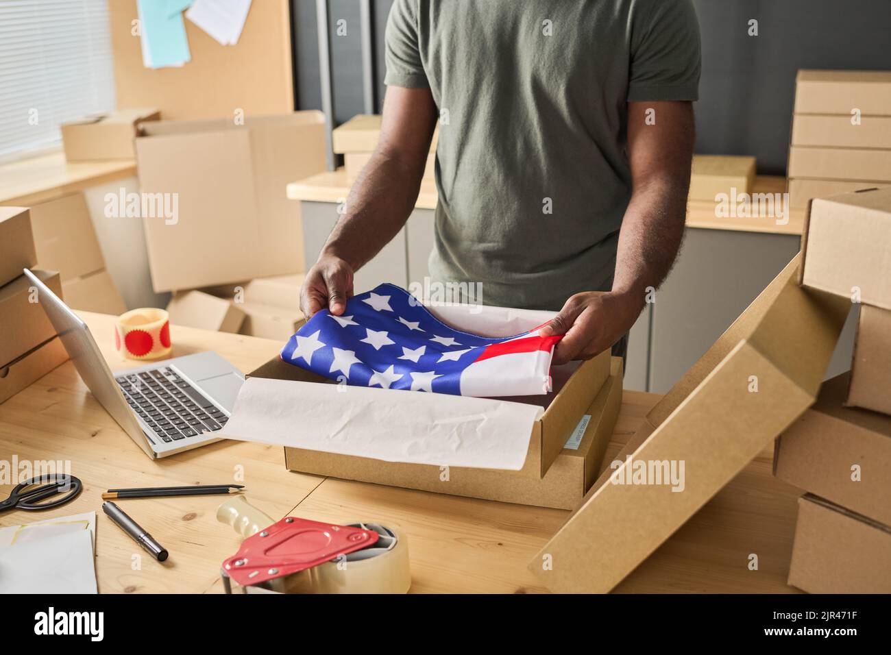 Close-up of African man packing American flag in cardboard box at table in warehouse Stock Photo
