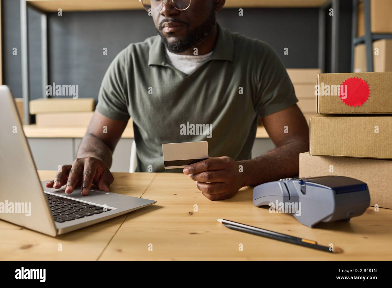 Close-up of African man using laptop to pay online with credit card at table in warehouse Stock Photo