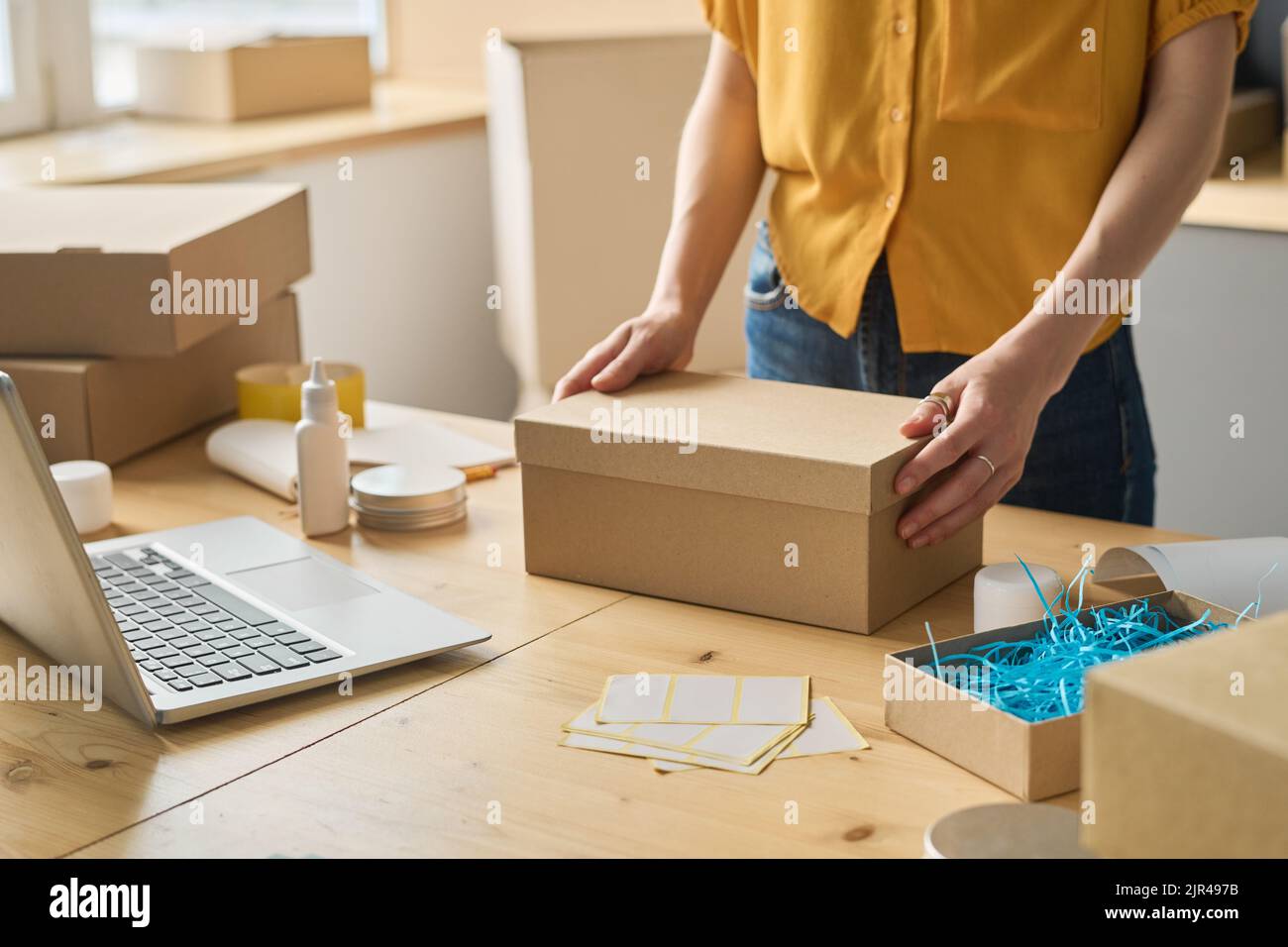 Close-up of warehouse worker packing online orders in cardboard boxes at table before shipping Stock Photo