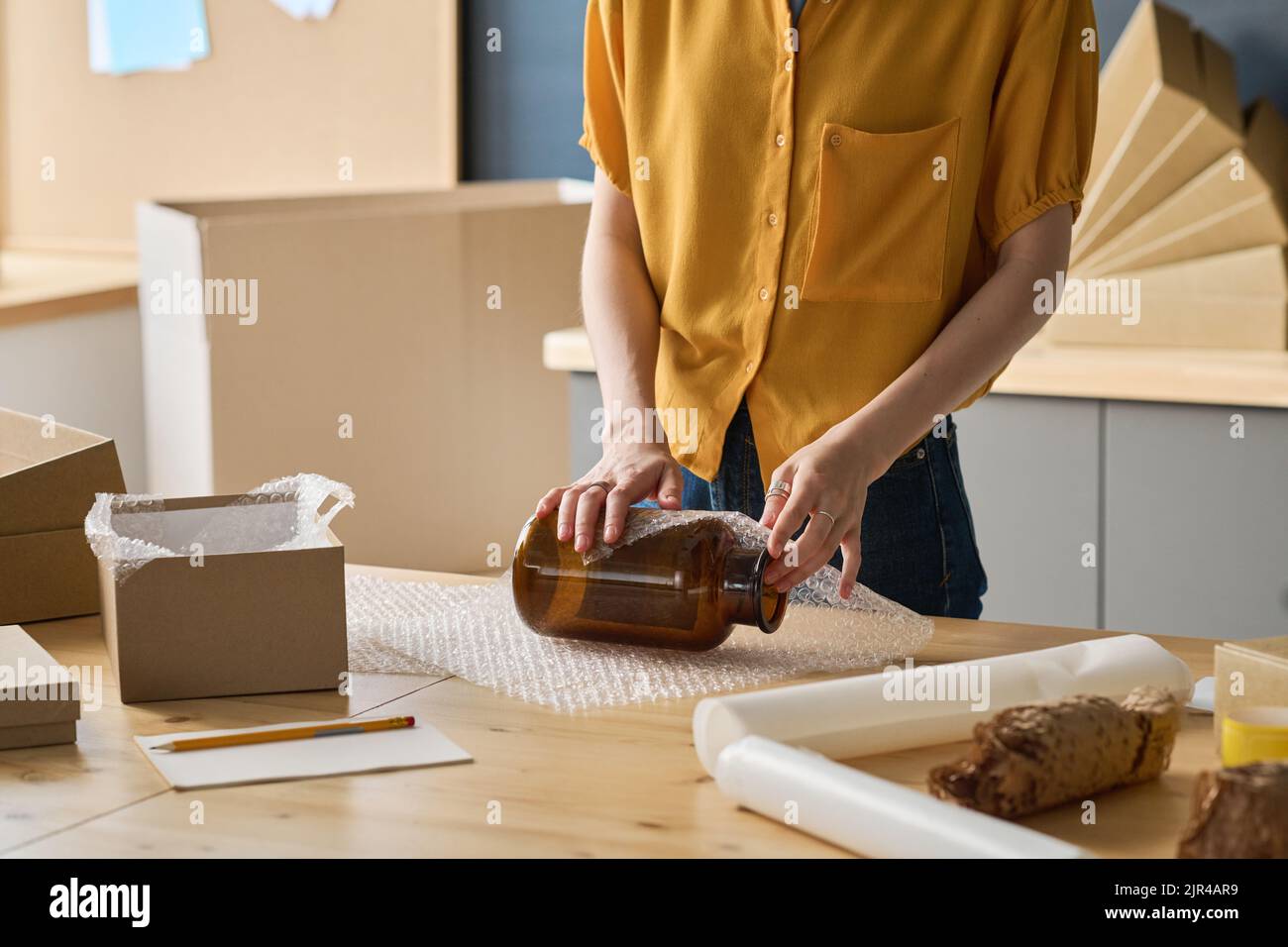 Close-up of female worker wrapping glass jar in packet to pack it in the box for delivery Stock Photo