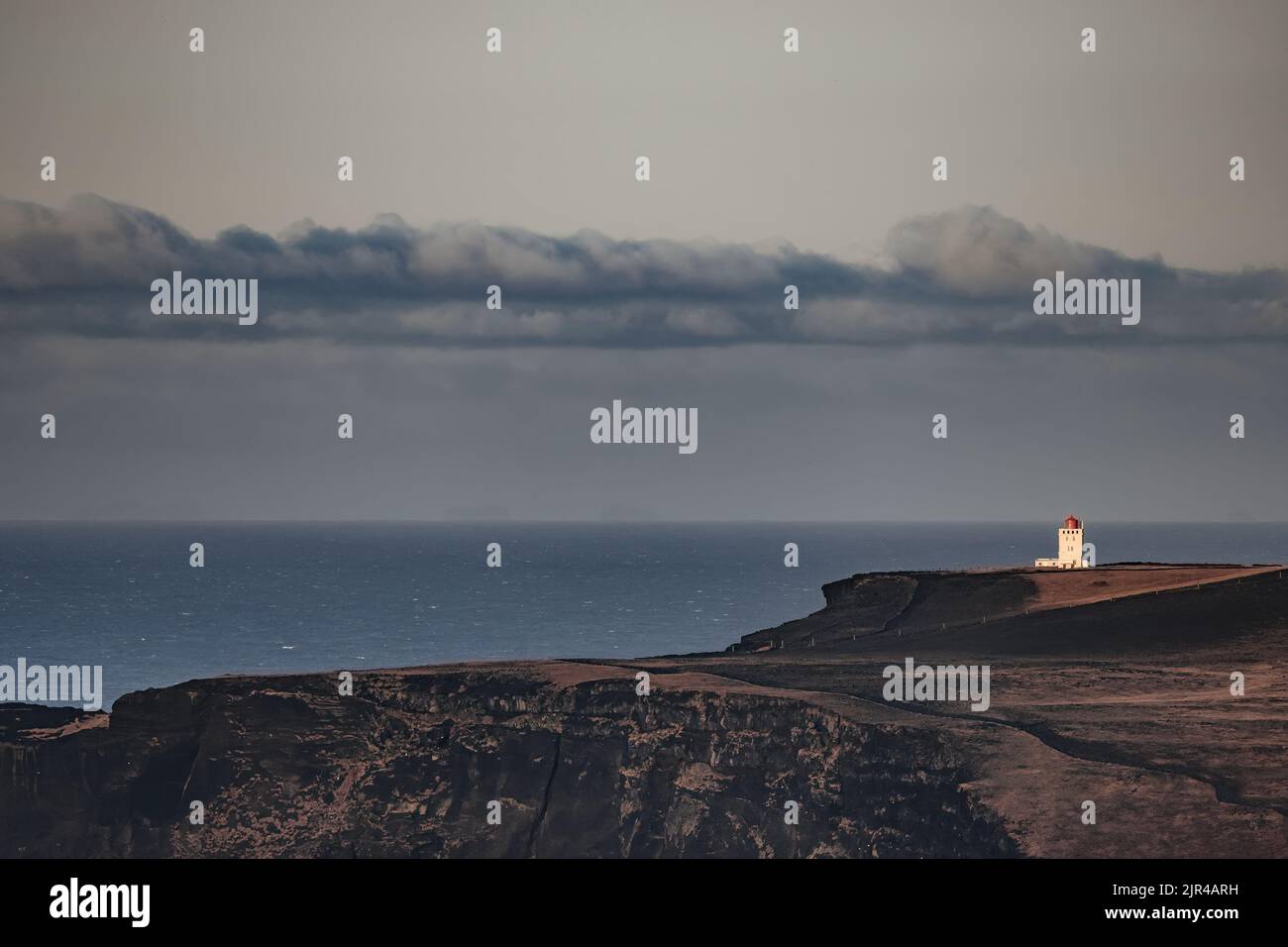 Dyrholaey Lighthouse stands on the rugged cliffs of the Southern iceland. Sea view in autumn with the Atlantic Ocean in the background. Stock Photo