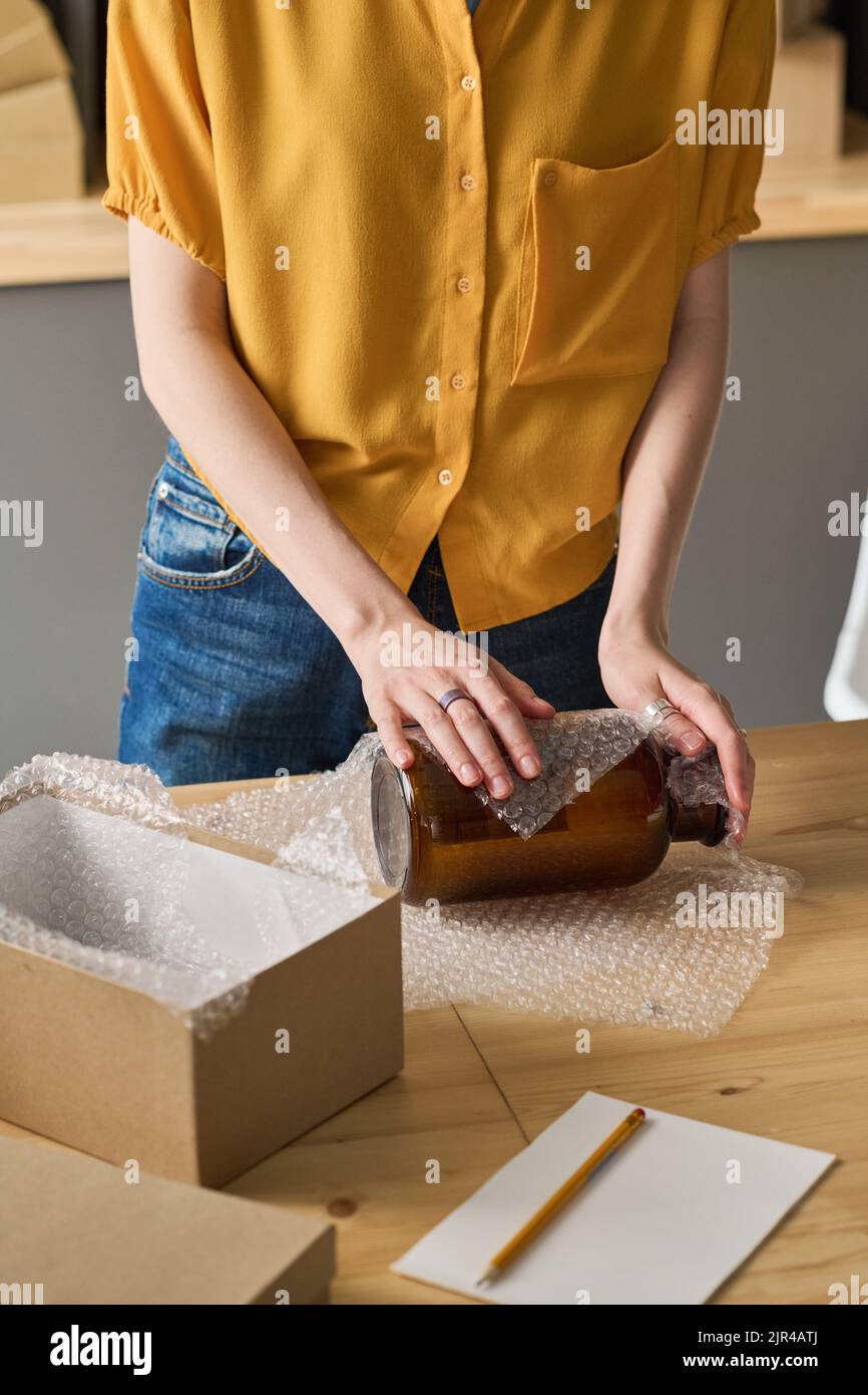 Close-up of young woman wrapping glass jar in packet, she making parcel for shipping Stock Photo