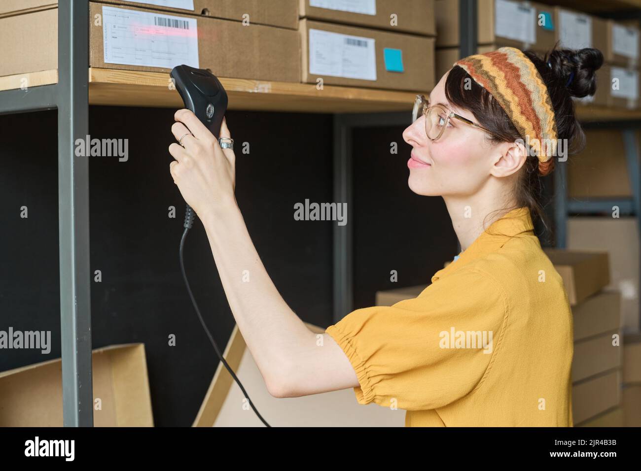 Young woman scanning parcels on shelf with scanner in warehouse Stock Photo