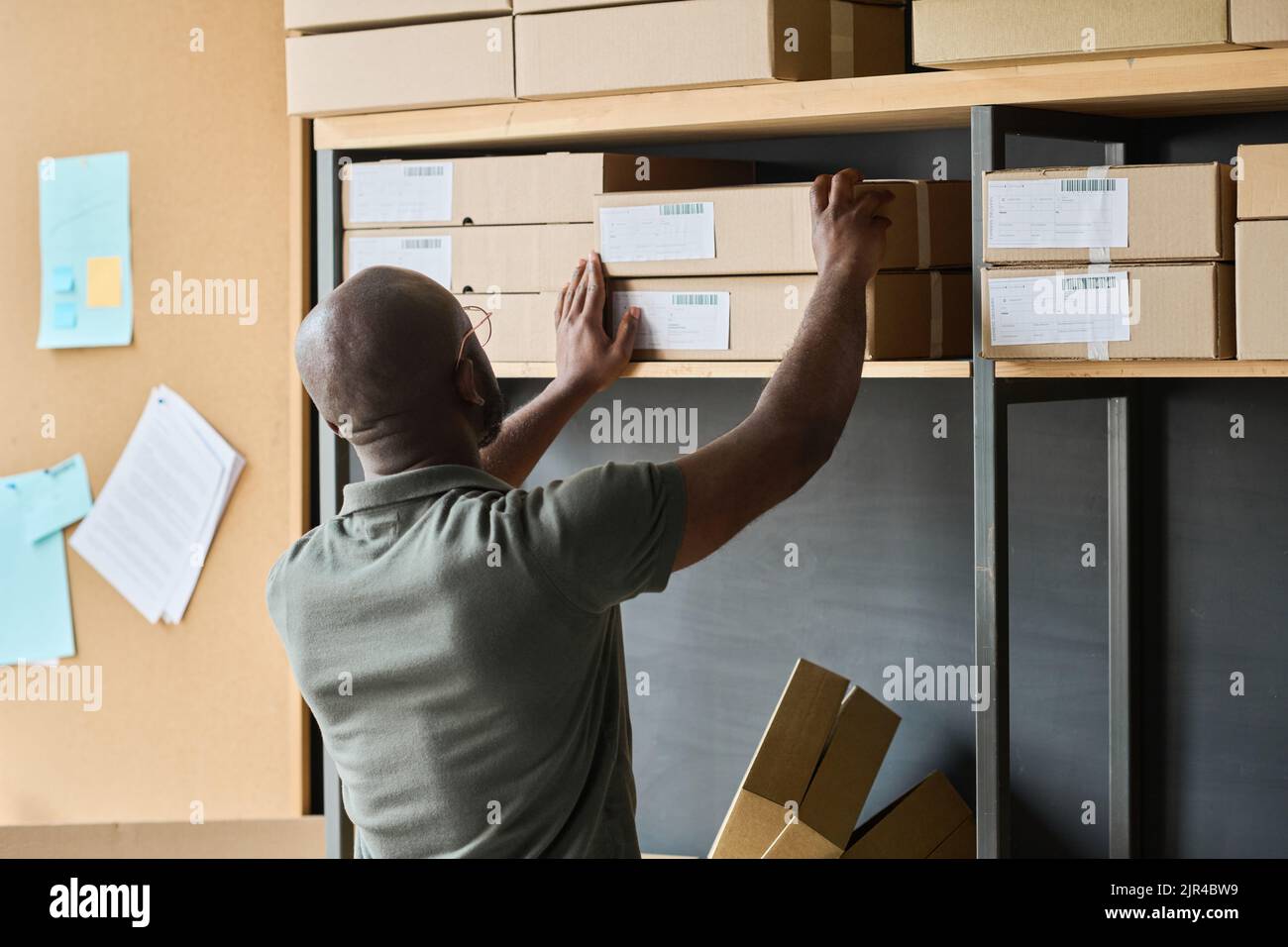 Rear view of African man putting finishes parcels in cardboard boxes on shelf during his work in warehouse Stock Photo