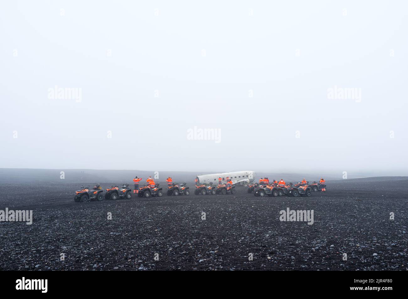 Tourists in orange overalls on quad bikes near the Abandoned wreck of a DC Plane on Solheimasandur in Iceland on a misty day Stock Photo