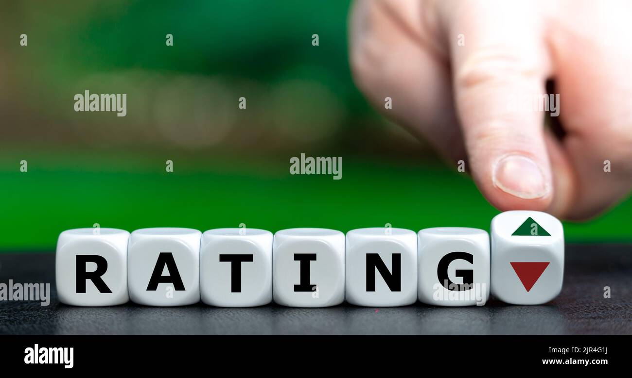 Hand turns dice and changes the direction of an arrow from down to up next to the word 'rating'. Symbol for a positive rating. Stock Photo