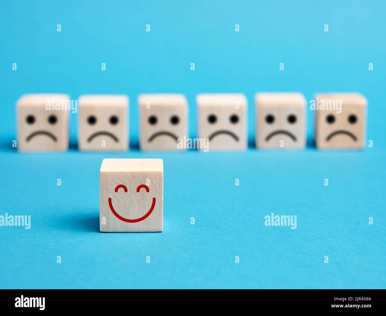 Wooden cube with smiling happy positive face stands out from the unhappy negative or sad faces. Good or positive customer rating, user review and feed Stock Photo