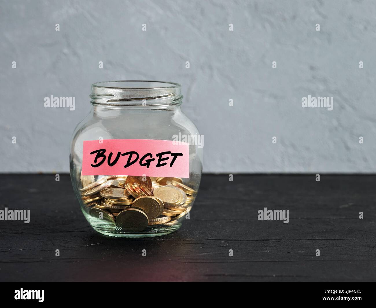 Glass jar with coins and the word budget on a label. Accumulating money for the family budget or education costs. Money saving and investment. Stock Photo