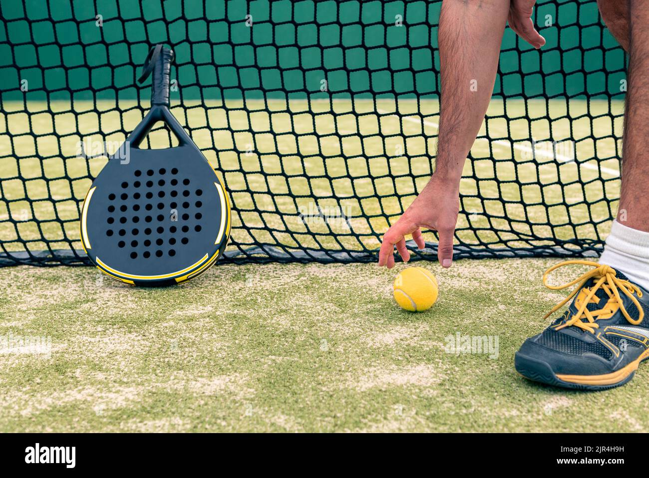 Monitor of padel holding a yellow ball near racket with copy space. Class to student on outdoor tennis court. Man paddel player playing a match in the Stock Photo