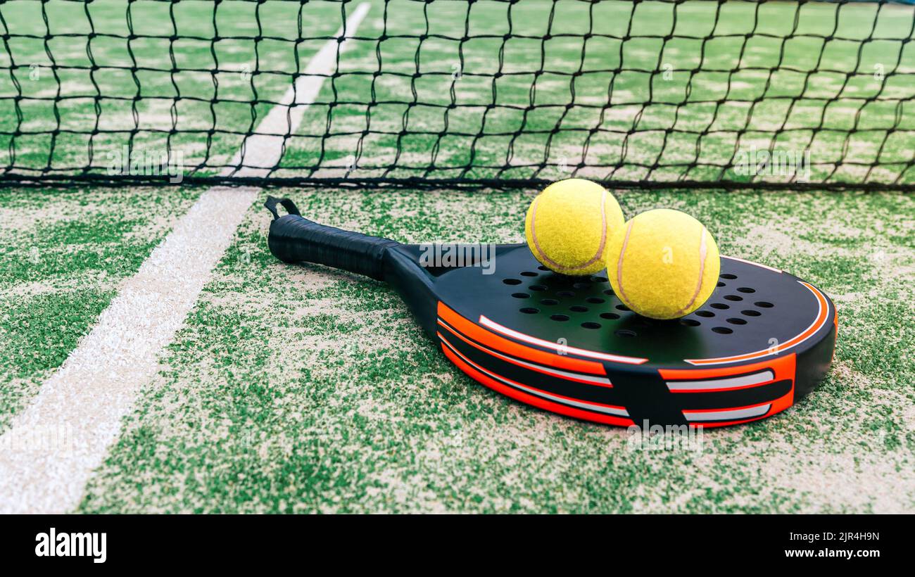 Yellow balls on top of the padel racket and behind net on a green court grass turf outdoors. Paddle is a racquet game. Professional sport concept with Stock Photo