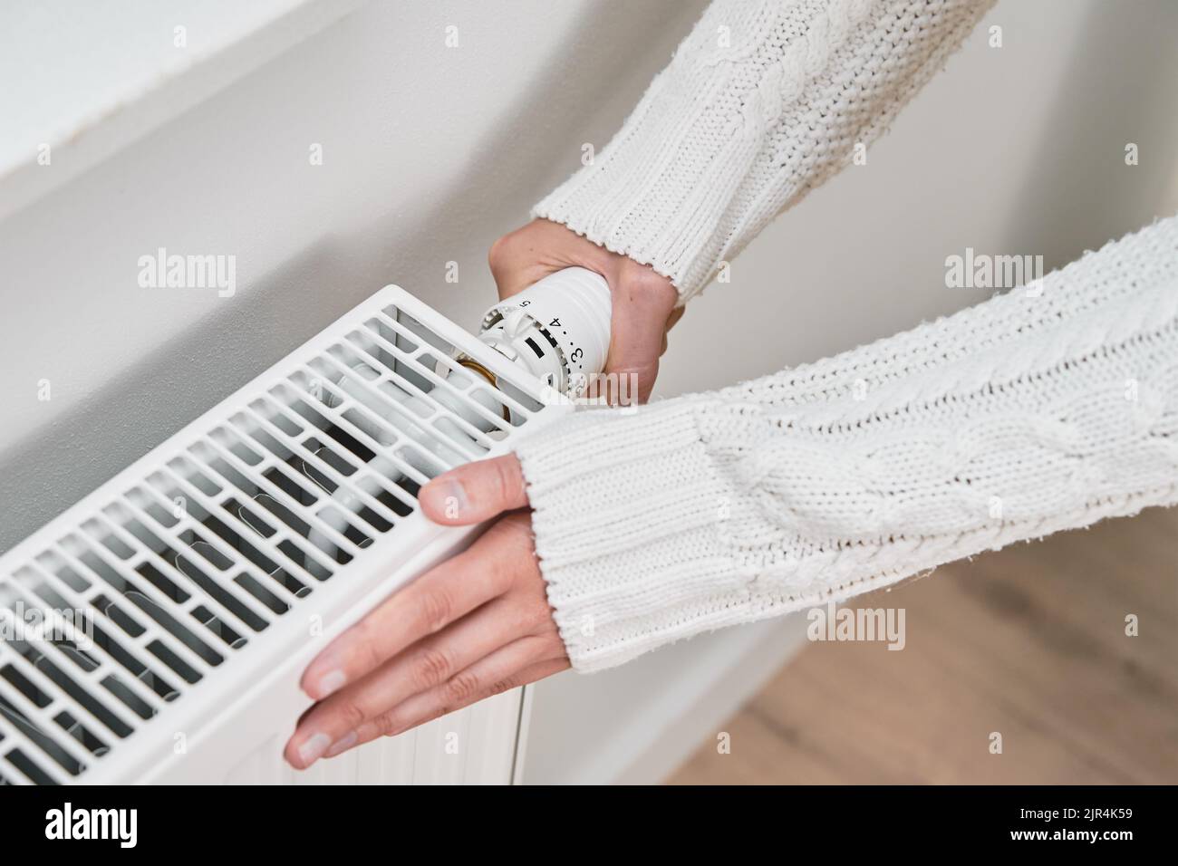 Woman adjusting temperature on heating radiator, Energy crisis concept in Europe, Rising costs in private households for gas bill due to inflation and Stock Photo