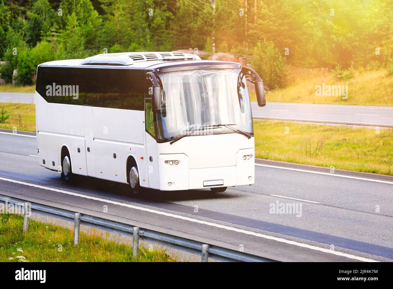White coach bus traveling at speed on motorway towards golden sunlight in the morning. No people, copy space right of image. Stock Photo