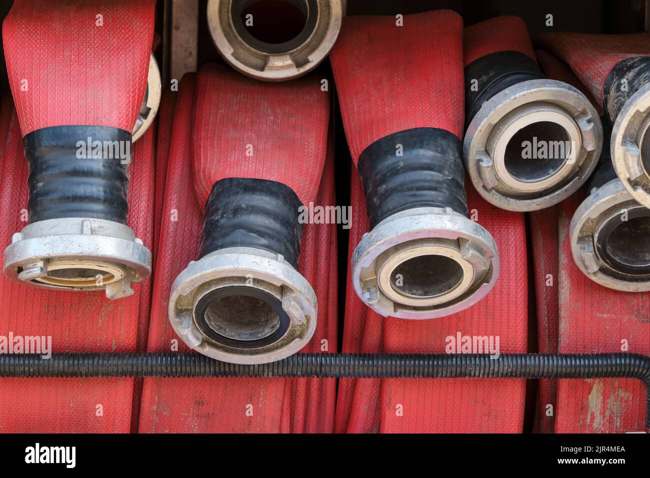 Closeup of red coiled water hoses with metal connections on a fire