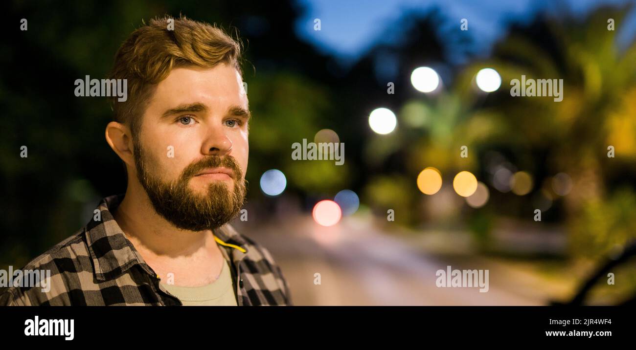 Banner portrait of man standing in night city street with bokeh street lights in background. Confident lonely guy. Close-up portrait Stock Photo