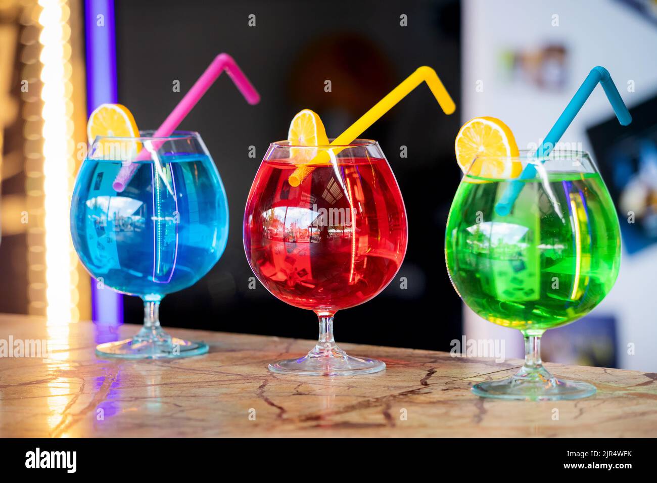 Three colorful bright cocktails with a straw and a slice of lemon. Chemical composition and unhealthy alcohol Stock Photo