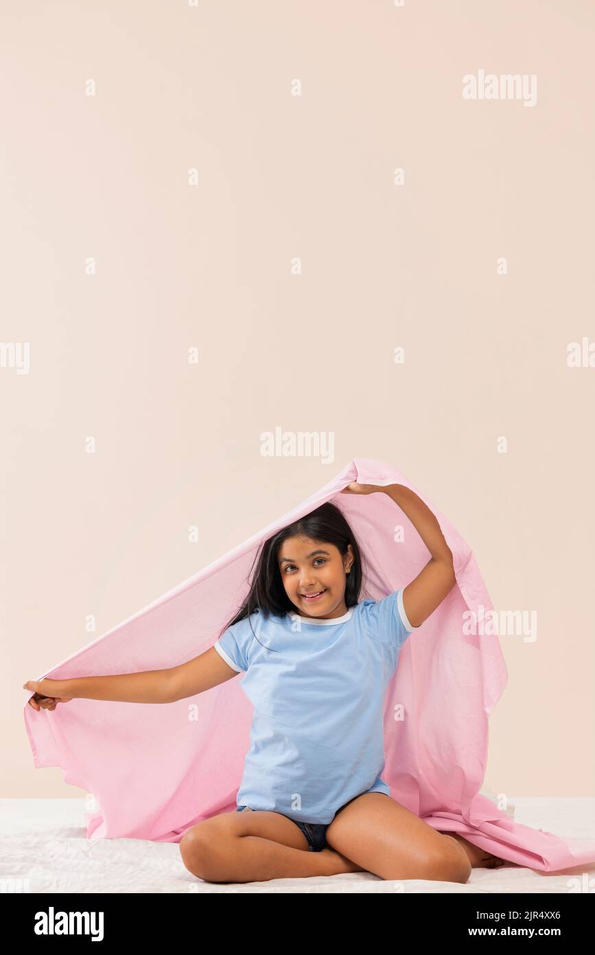 Portrait of a girl sitting on bed with holding a blanket over her head